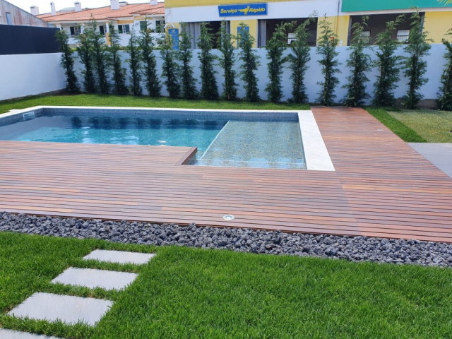 Piscina de skimmer, revestida a pastilha/mosaico de vidro, bordadura em pedra bujardada e pavimento em madeira ipê